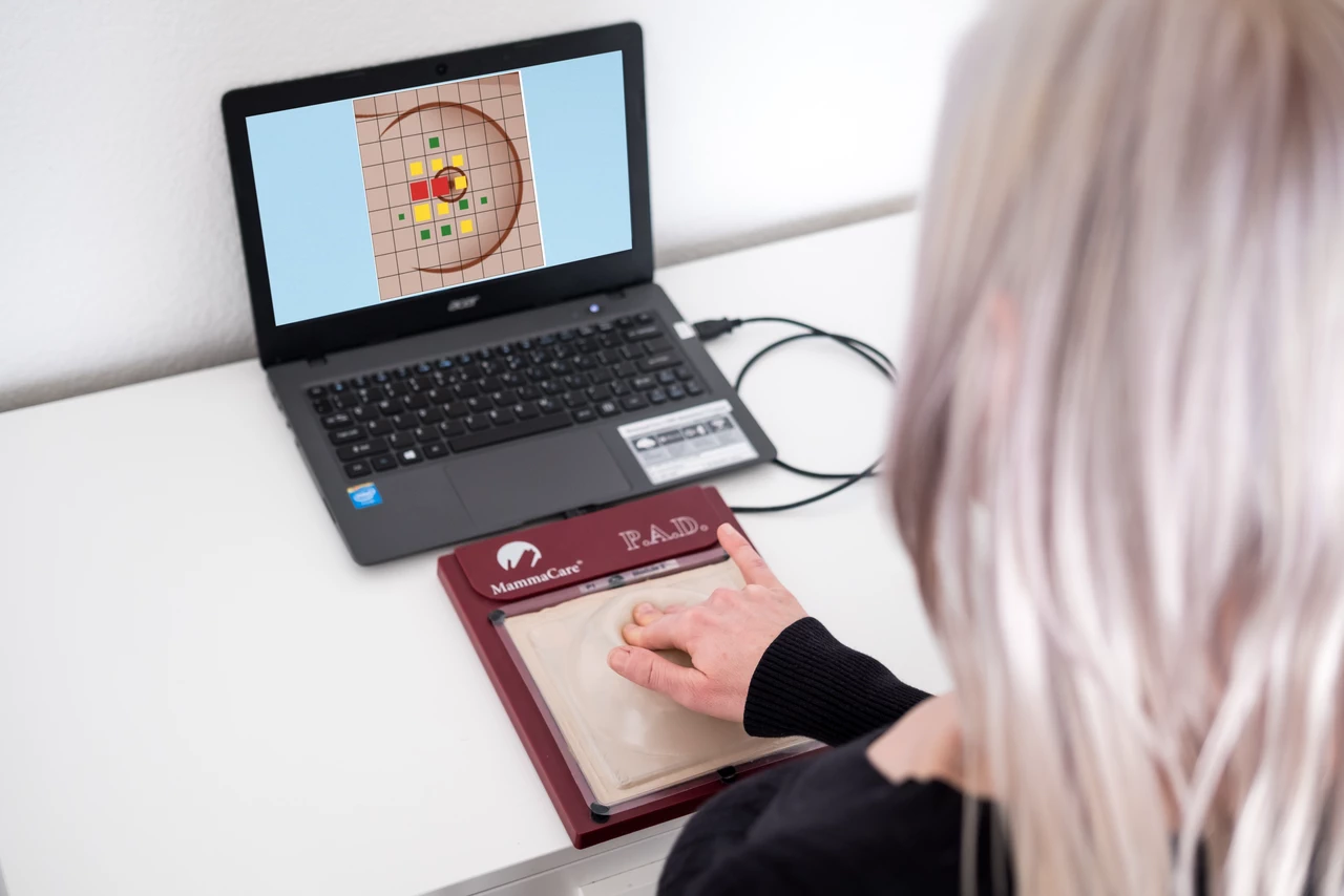 Healthcare provider completing AI-guided breast exam training shot from over the left shoulder looking down at a laptop and a breast model on the simulator pad